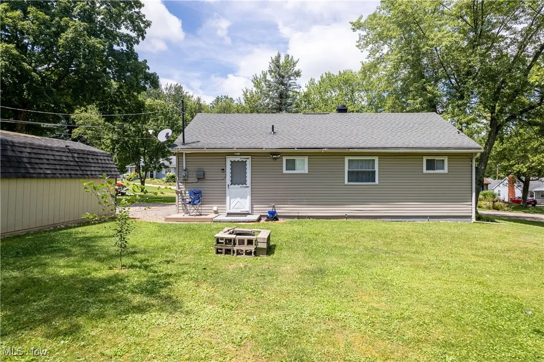 Rear view of property featuring a lawn, a shingled roof, and an outdoor structure