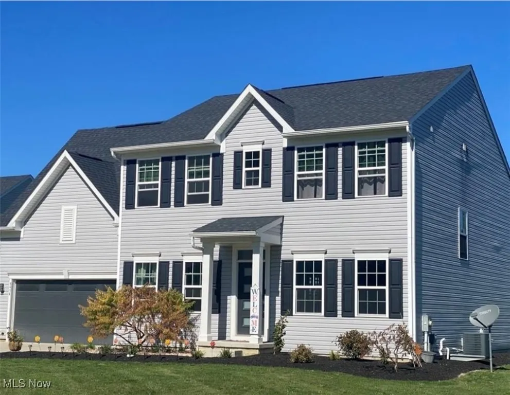 Colonial-style house with a shingled roof, a garage, and a front yard