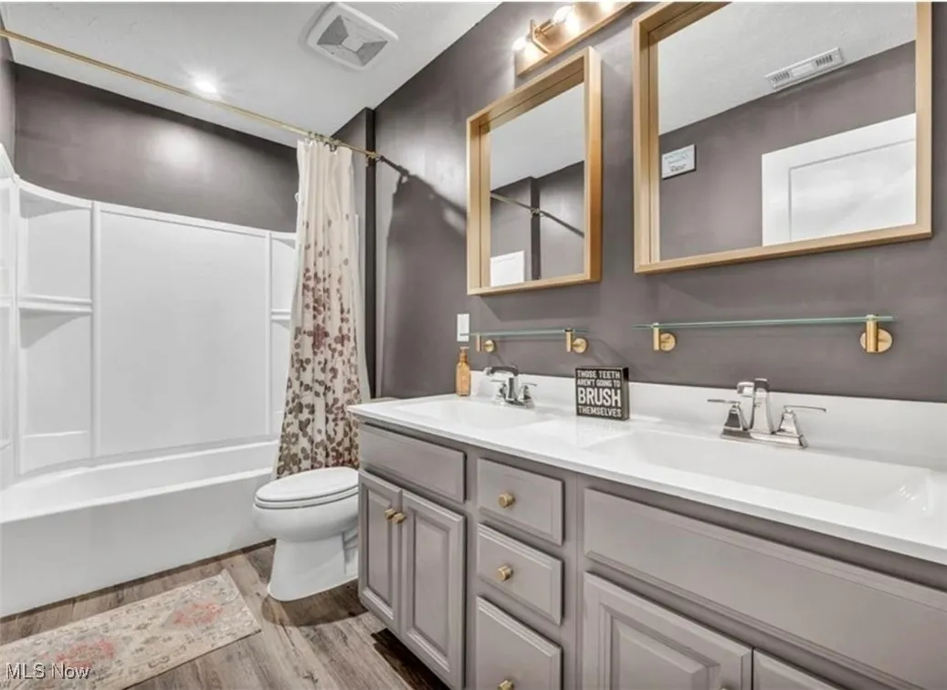 Full bath with double vanity, shower / bath combo with shower curtain, and wood finished floors
