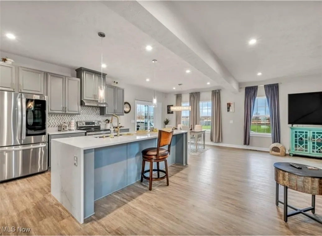 Kitchen with beamed ceiling, stainless steel appliances, gray cabinets, a spacious island, and tasteful backsplash