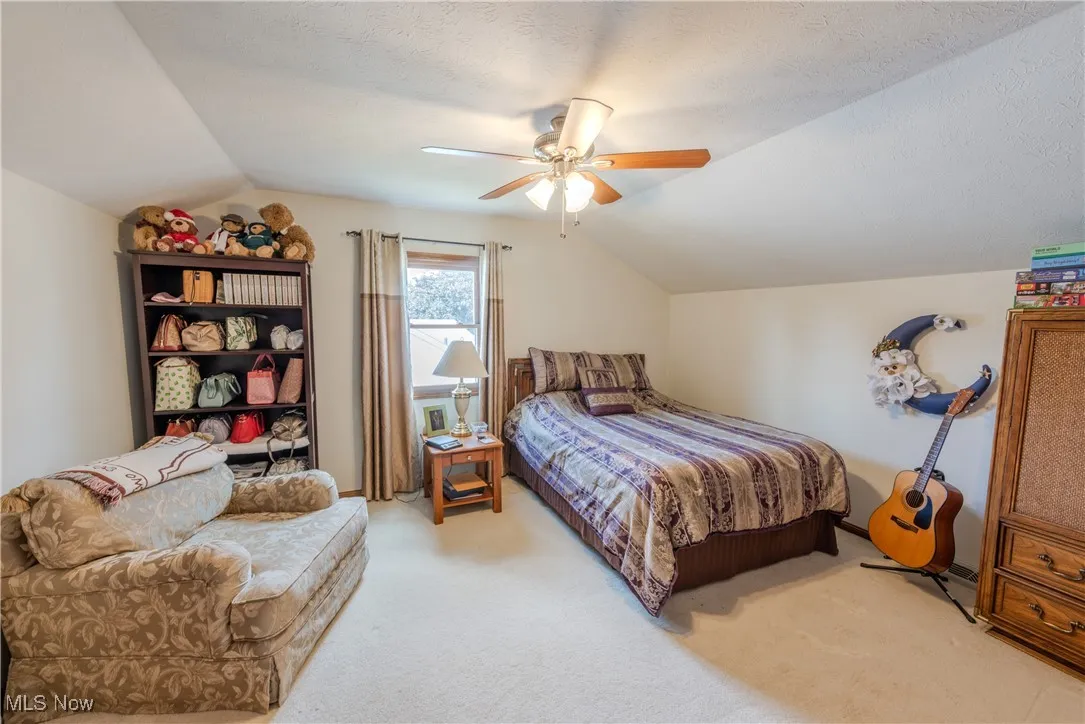 Bedroom with vaulted ceiling, light colored carpet, and ceiling fan