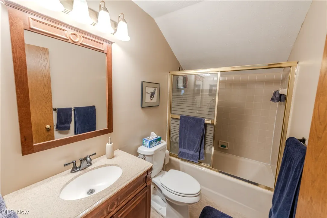 Full bath with vanity, vaulted ceiling, and combined bath / shower with glass door