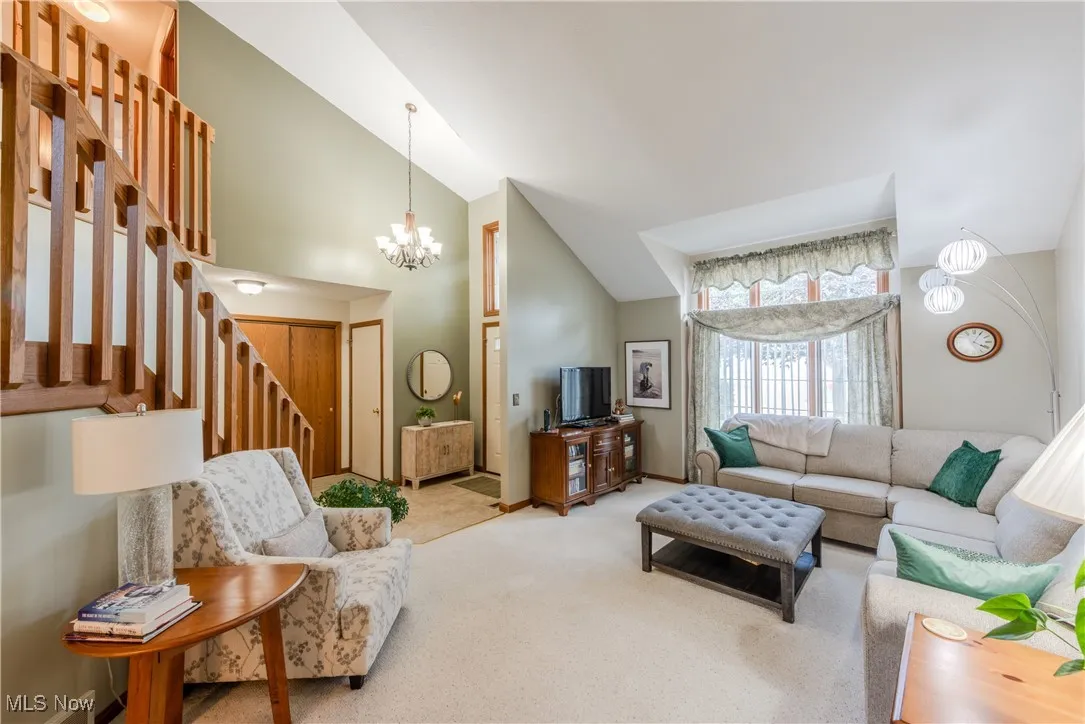 Living room featuring carpet, a chandelier, high vaulted ceiling, and stairway