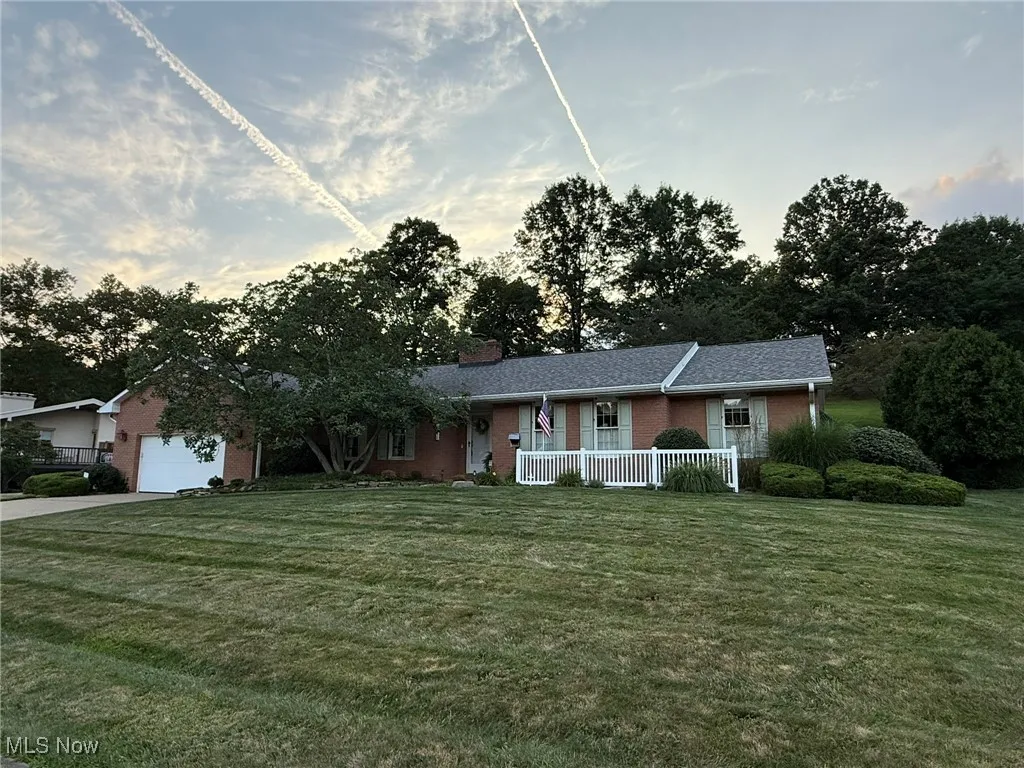Ranch-style house featuring covered porch, brick siding, a front lawn, and an attached garage