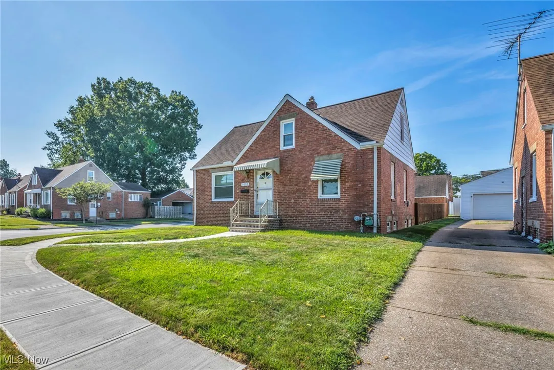View of front of home with brick siding, a front lawn, a chimney, a garage, and an outbuilding