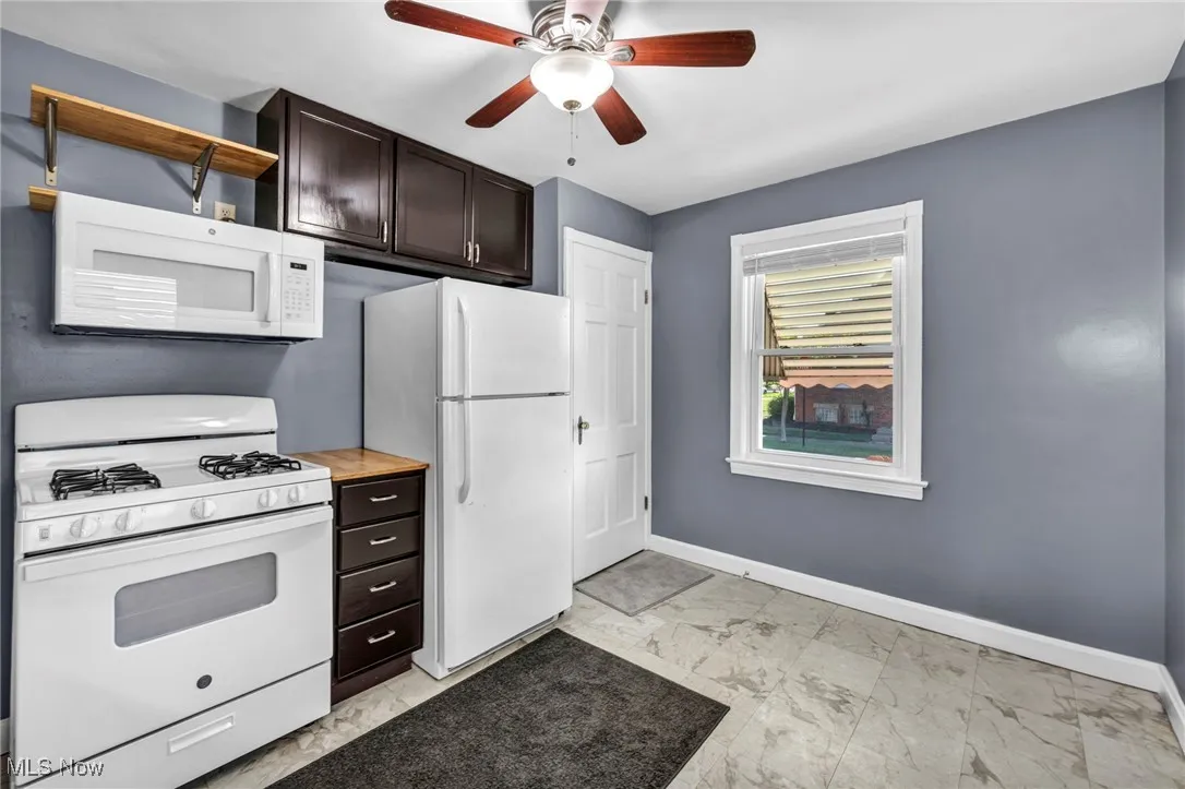 Kitchen featuring white appliances, light marble finish floors, a ceiling fan, dark brown cabinetry, and light countertops