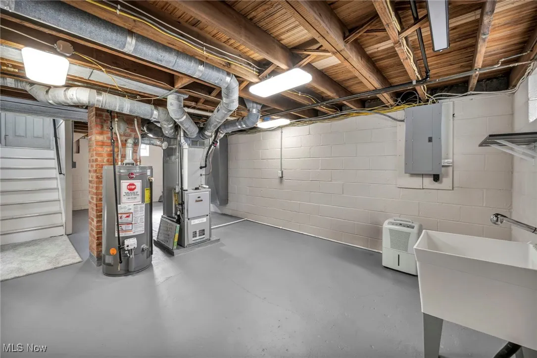 Unfinished basement featuring electric panel, water heater, stairway, and heating unit