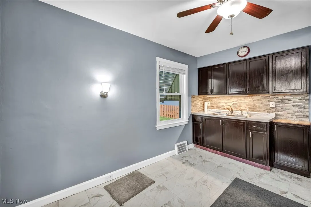 Bar area with light marble finish floors, backsplash, and a ceiling fan