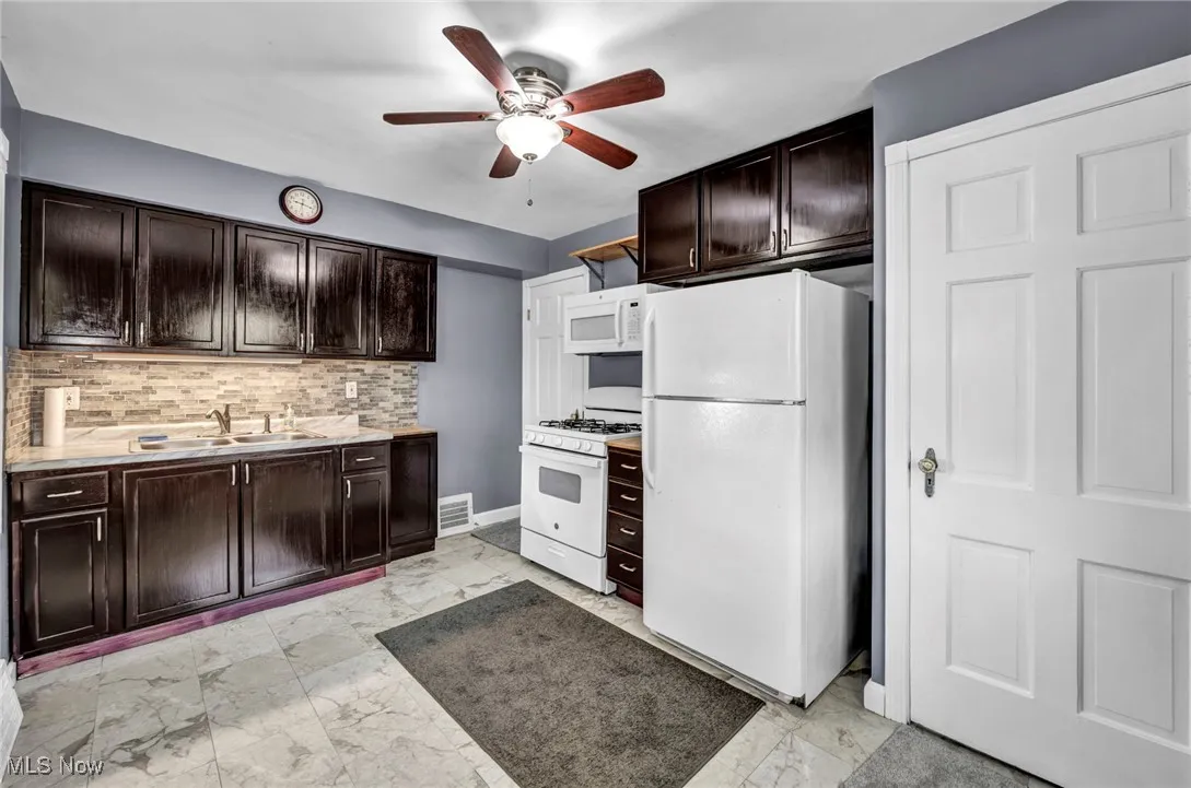 Kitchen featuring white appliances, a ceiling fan, light marble finish floors, dark brown cabinetry, and light countertops