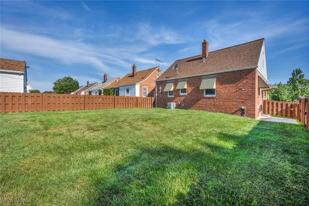 Rear view of house featuring brick siding, a fenced backyard, a chimney, and a shingled roof