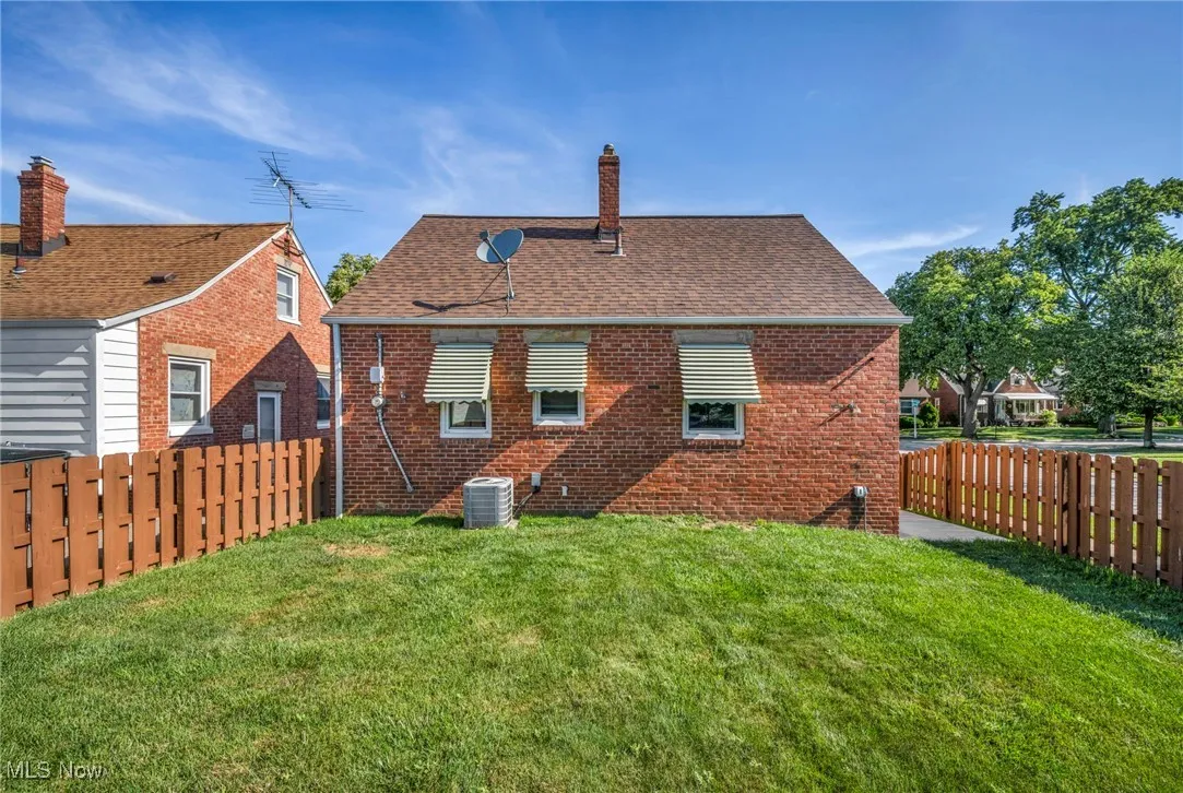 Rear view of house featuring a chimney, a shingled roof, brick siding, and a fenced backyard