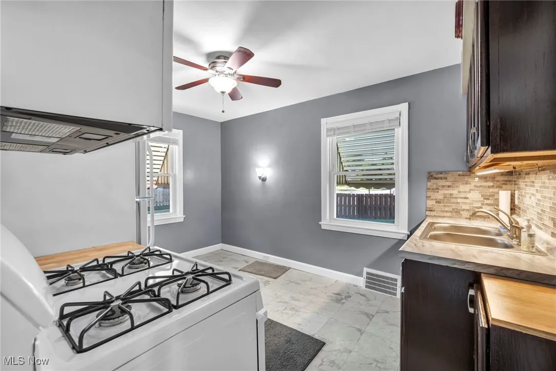 Kitchen with white gas range oven, light marble finish floors, a ceiling fan, and healthy amount of natural light