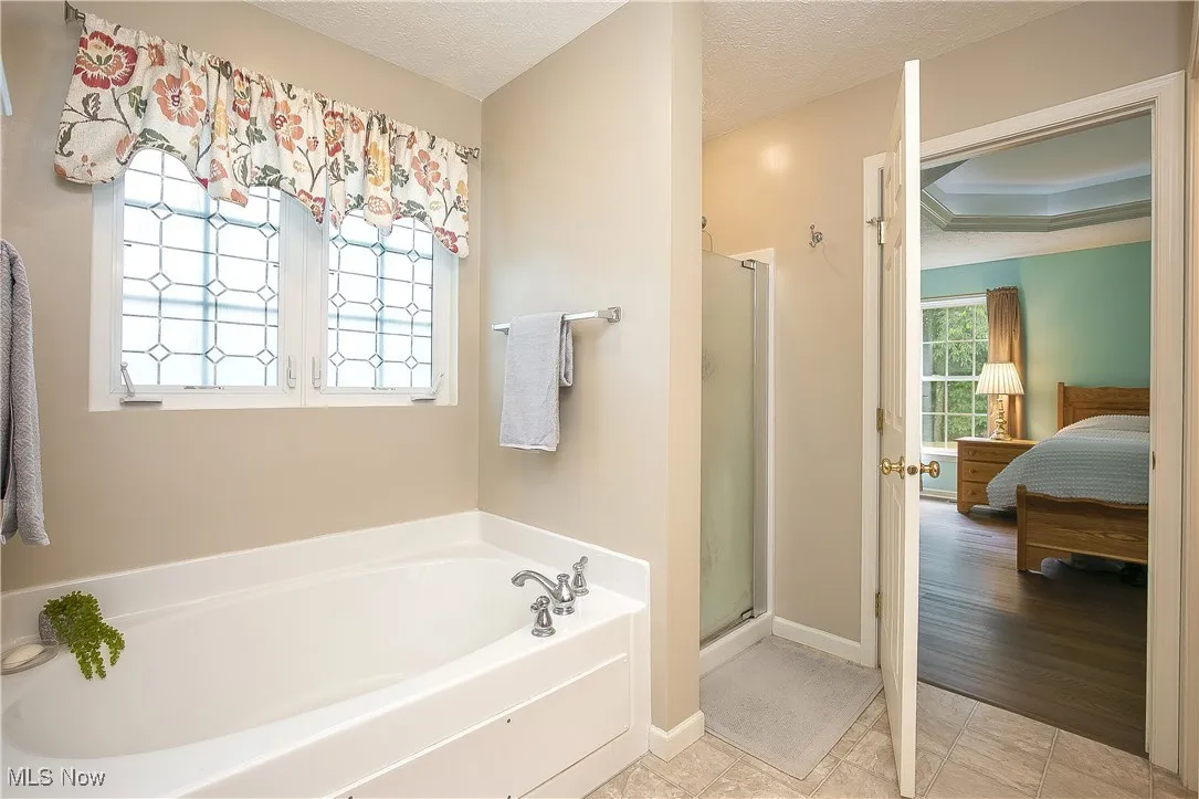 Bathroom featuring connected bathroom, a garden tub, a stall shower, a textured ceiling, and ornamental molding