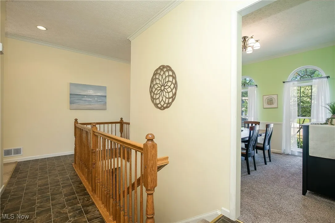 Corridor with an upstairs landing, ornamental molding, a textured ceiling, and carpet