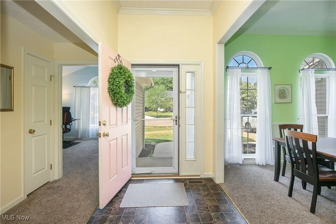 Entryway with dark carpet, crown molding, stone finish flooring, and healthy amount of natural light