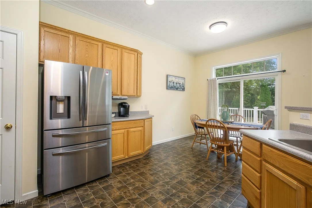 Kitchen with stainless steel fridge, crown molding, a textured ceiling, light countertops, and stone finish flooring