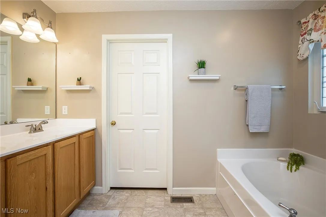 Bathroom featuring a garden tub, double vanity, and a textured ceiling