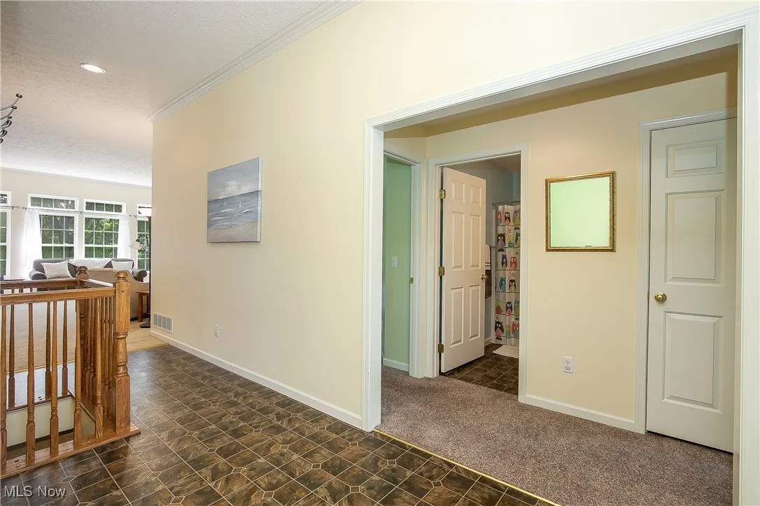 Hall with an upstairs landing, a textured ceiling, stone finish floors, dark colored carpet, and crown molding