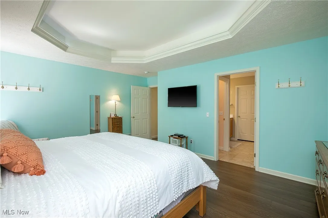 Bedroom with a raised ceiling, wood finished floors, and a textured ceiling