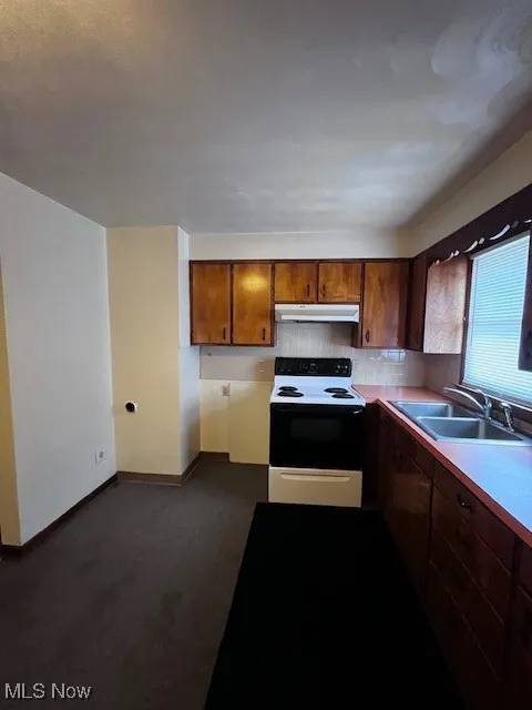 Kitchen with stove, light countertops, brown cabinetry, and ventilation hood