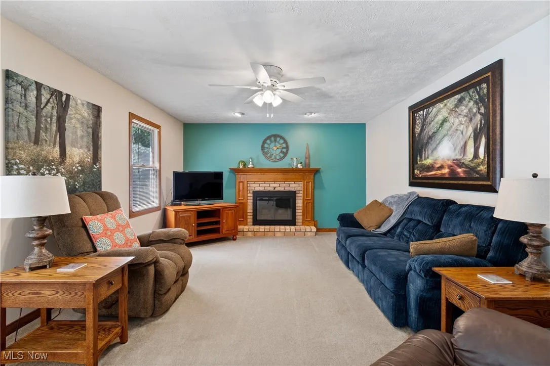 Living room with ceiling fan, light colored carpet, a fireplace, and a textured ceiling