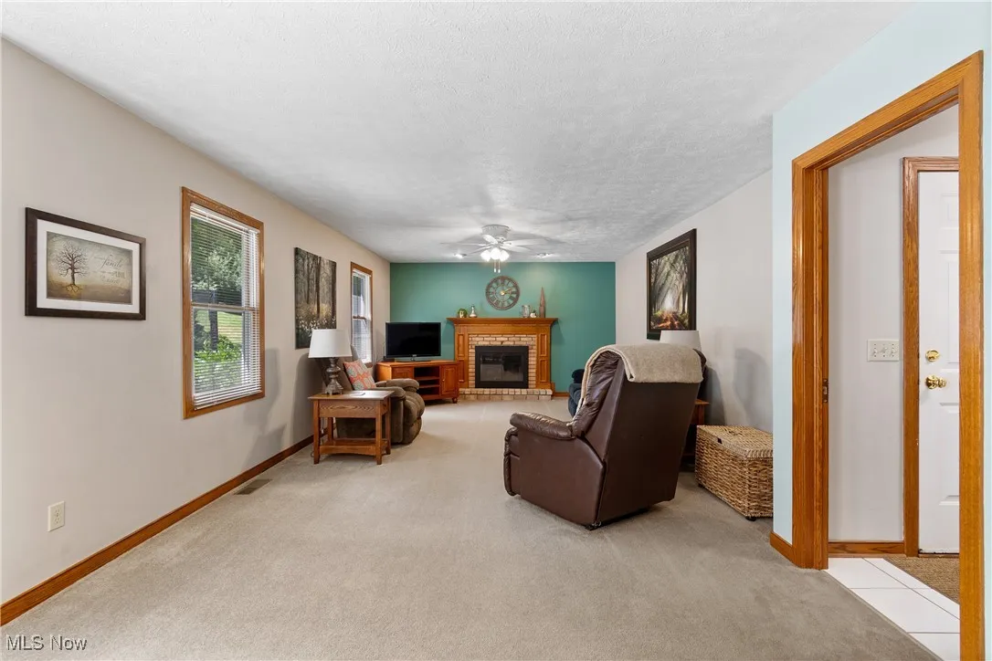 Living area with ceiling fan, a brick fireplace, carpet, and a textured ceiling