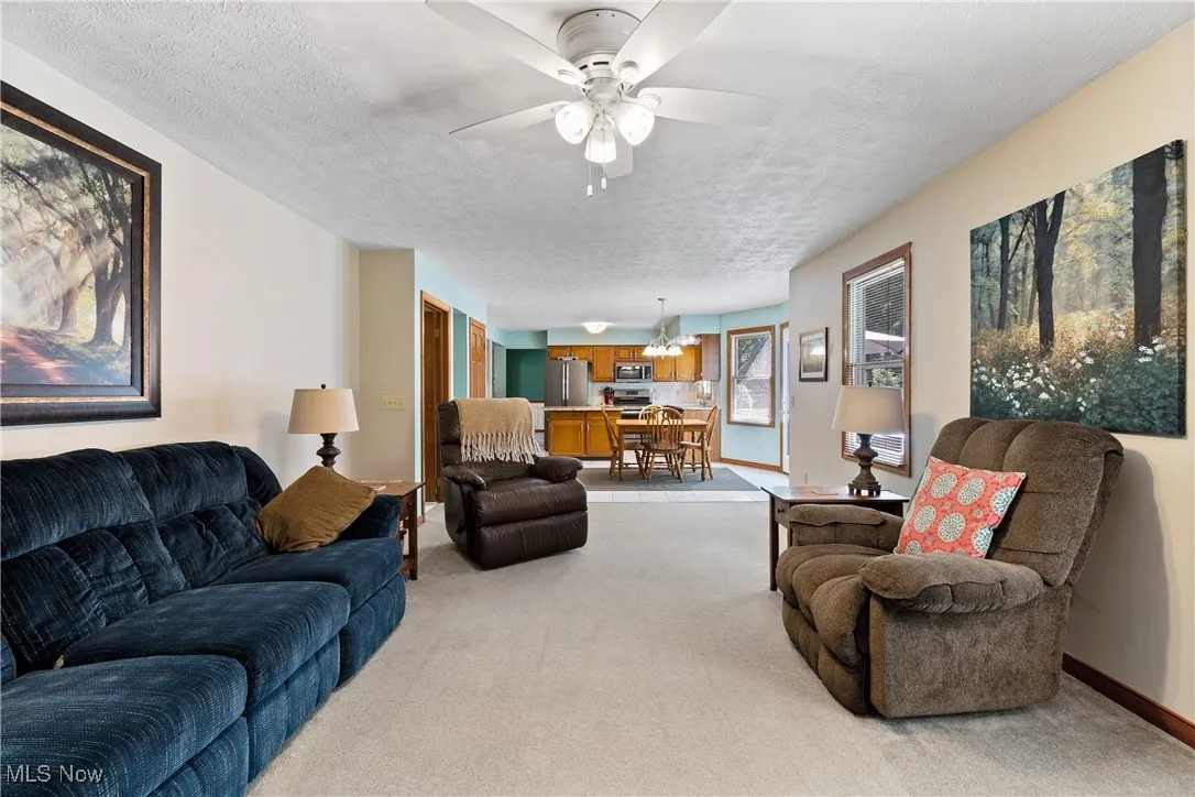 Living area featuring a textured ceiling, light colored carpet, and ceiling fan
