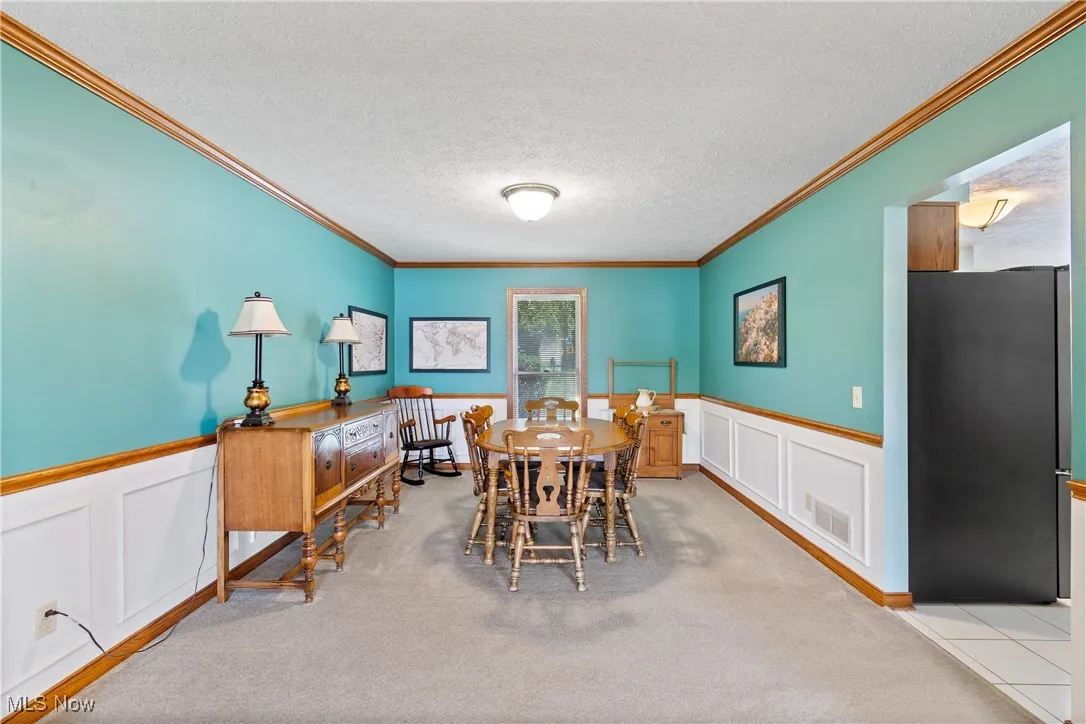 Dining space featuring a decorative wall, wainscoting, a textured ceiling, crown molding, and carpet floors