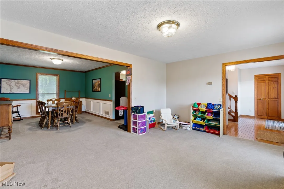 Carpeted dining area featuring a textured ceiling, a wainscoted wall, and ornamental molding