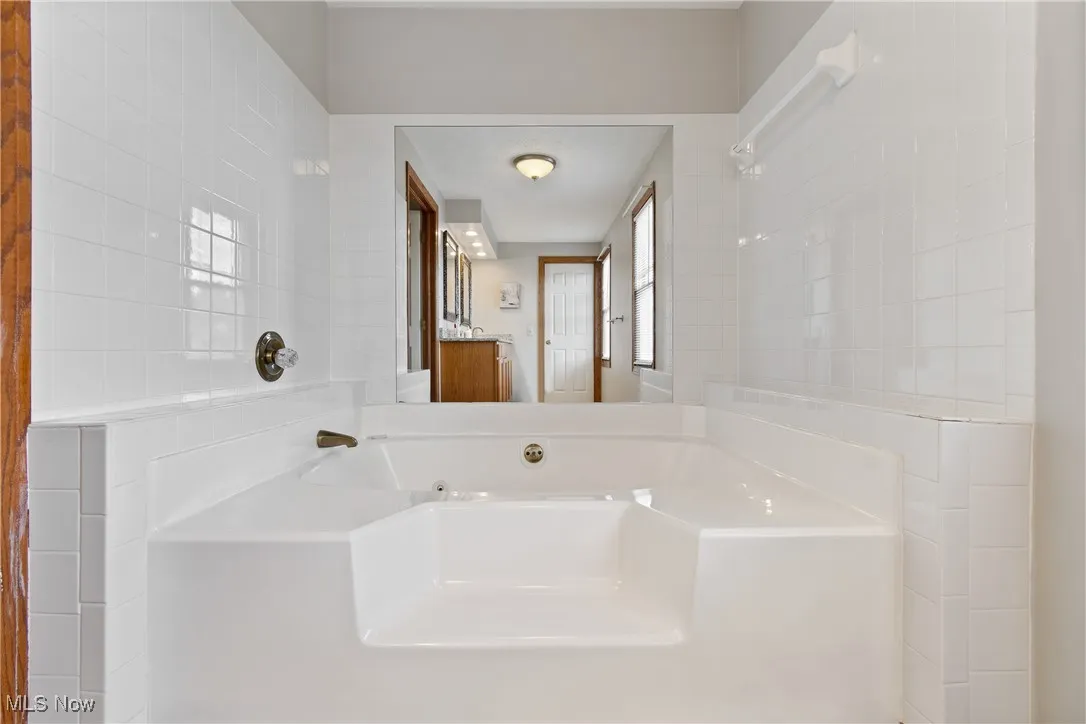 Full bath featuring a garden tub, vanity, and tile walls