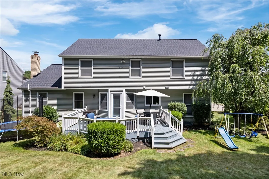 Rear view of property with a trampoline, roof with shingles, a yard, a wooden deck, and a playground