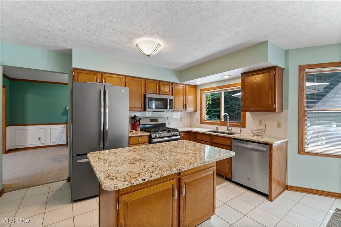 Kitchen with appliances with stainless steel finishes, brown cabinets, a kitchen island, a textured ceiling, and light tile patterned floors