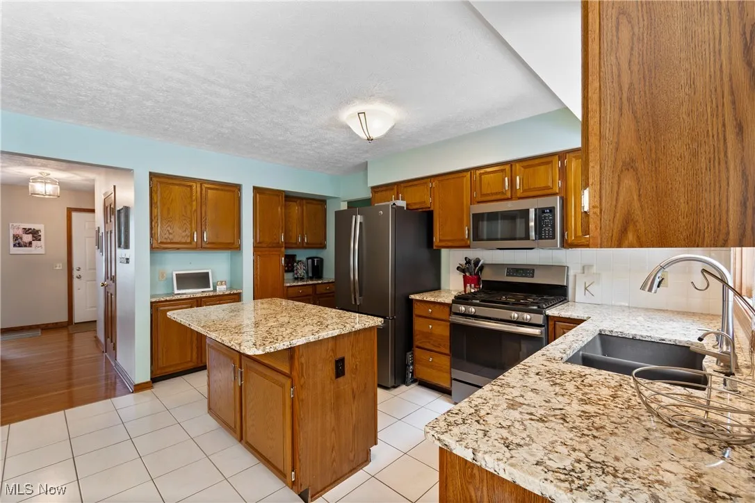 Kitchen featuring stainless steel appliances, a kitchen island, brown cabinetry, decorative backsplash, and a textured ceiling