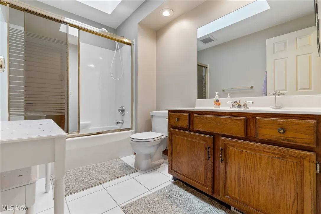 Bathroom with tile patterned floors, vanity, a skylight, shower / bath combination with glass door, and recessed lighting