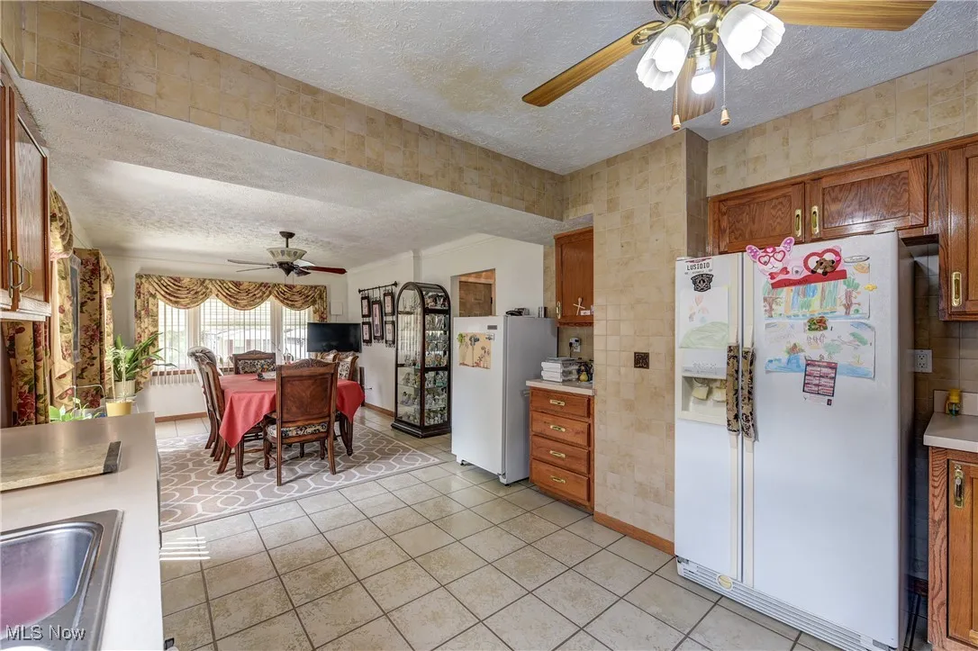 Kitchen featuring a ceiling fan, a textured ceiling, white refrigerator with ice dispenser, freestanding refrigerator, and light countertops