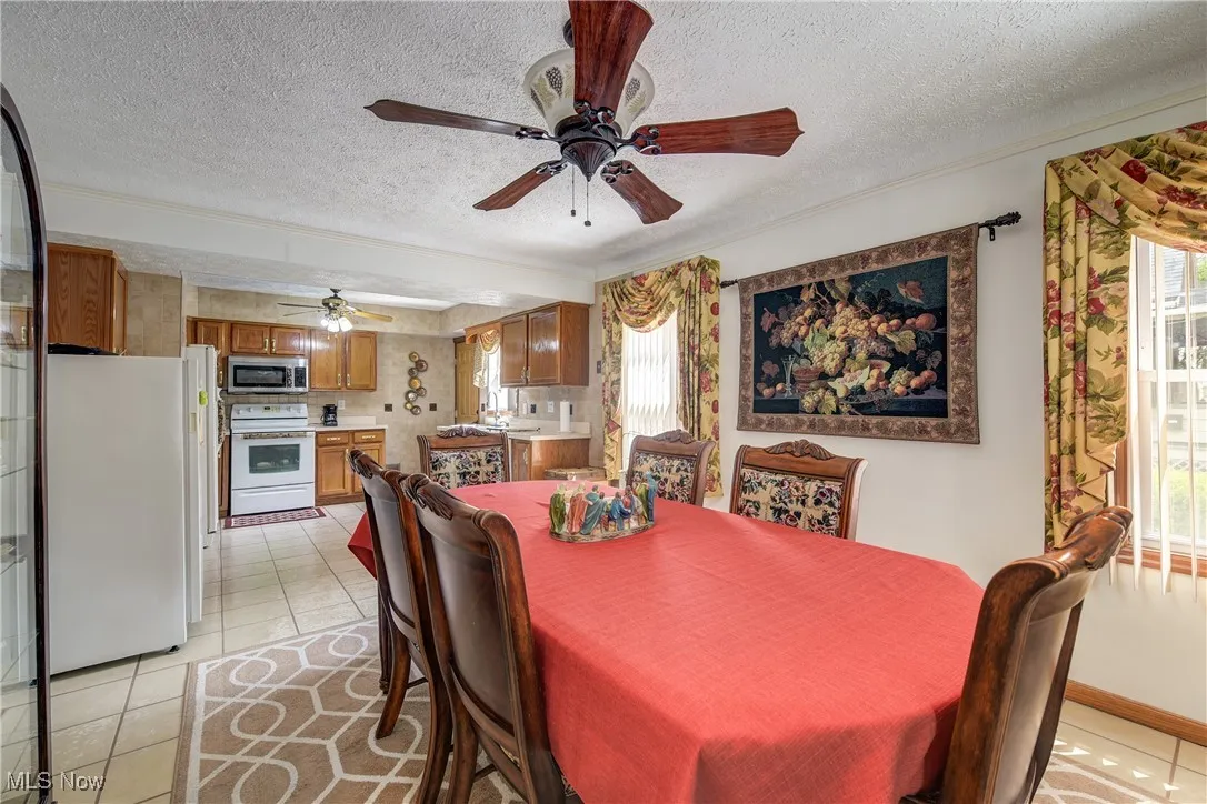 Dining area featuring crown molding, a textured ceiling, light tile patterned floors, and ceiling fan