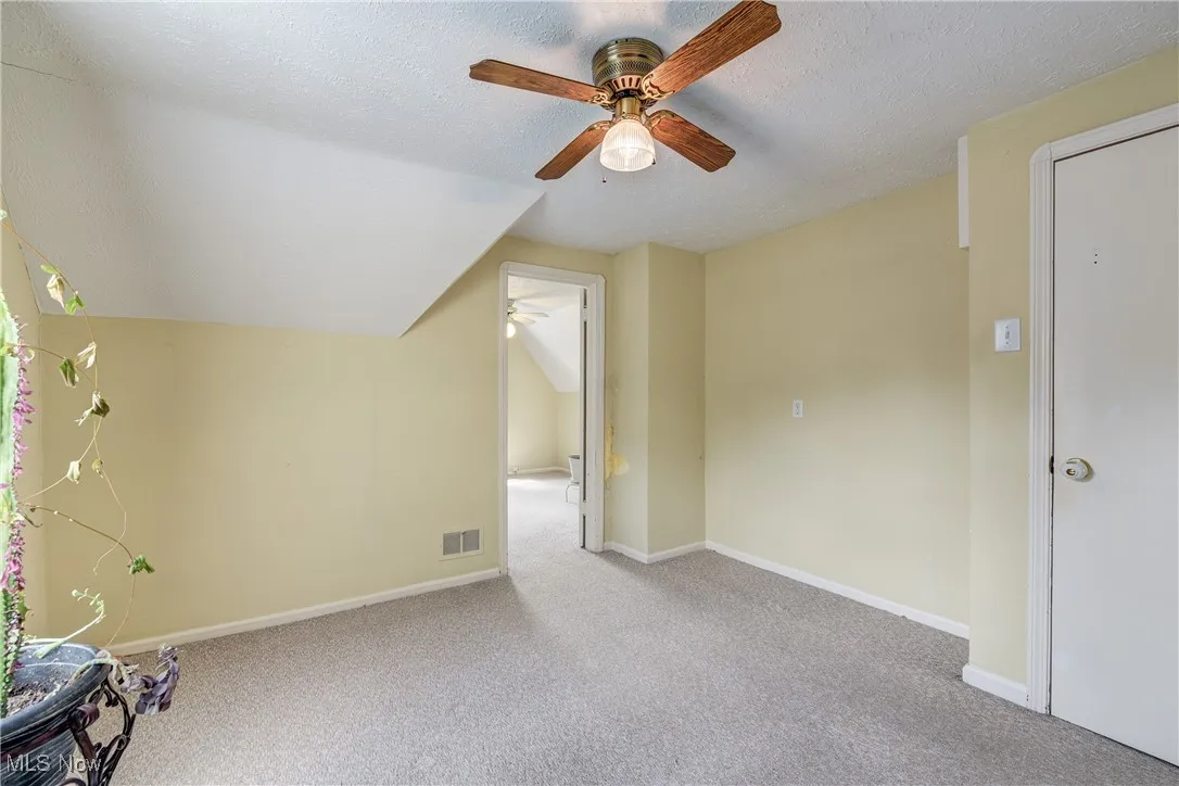 Carpeted empty room with a textured ceiling, a ceiling fan, and lofted ceiling