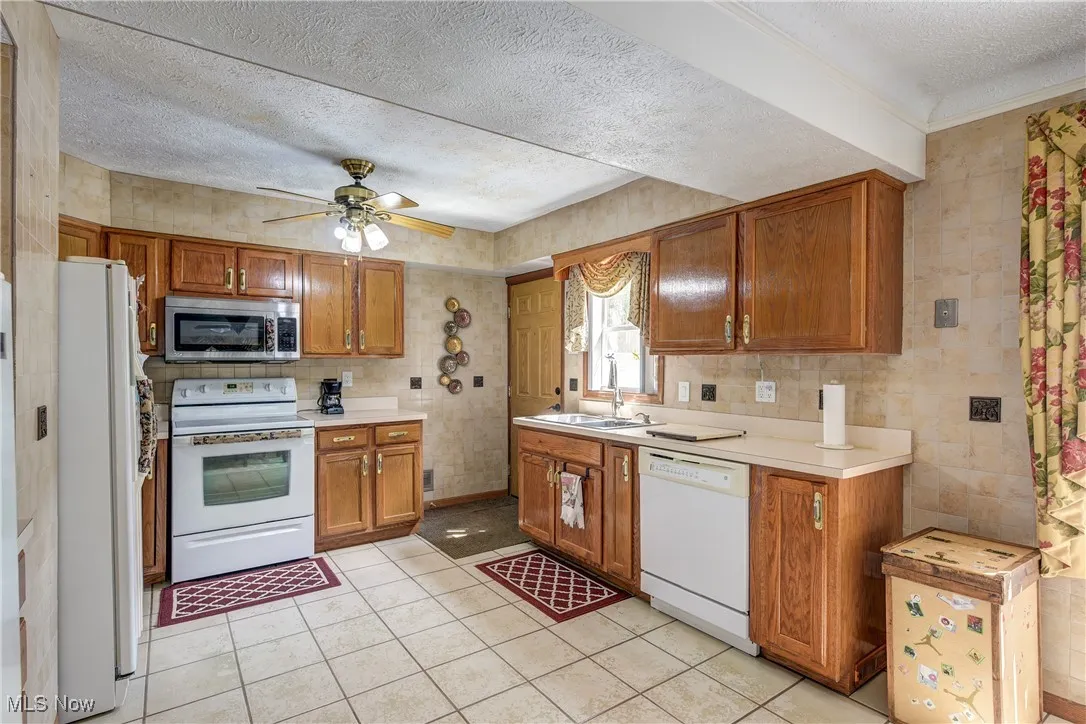 Kitchen featuring a textured ceiling, white appliances, brown cabinets, light countertops, and a ceiling fan