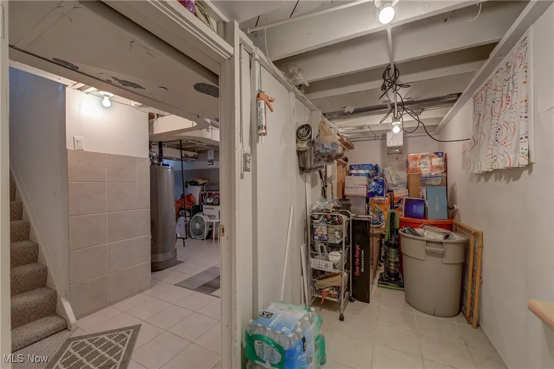 Below grade area featuring light tile patterned flooring, stairway, and water heater