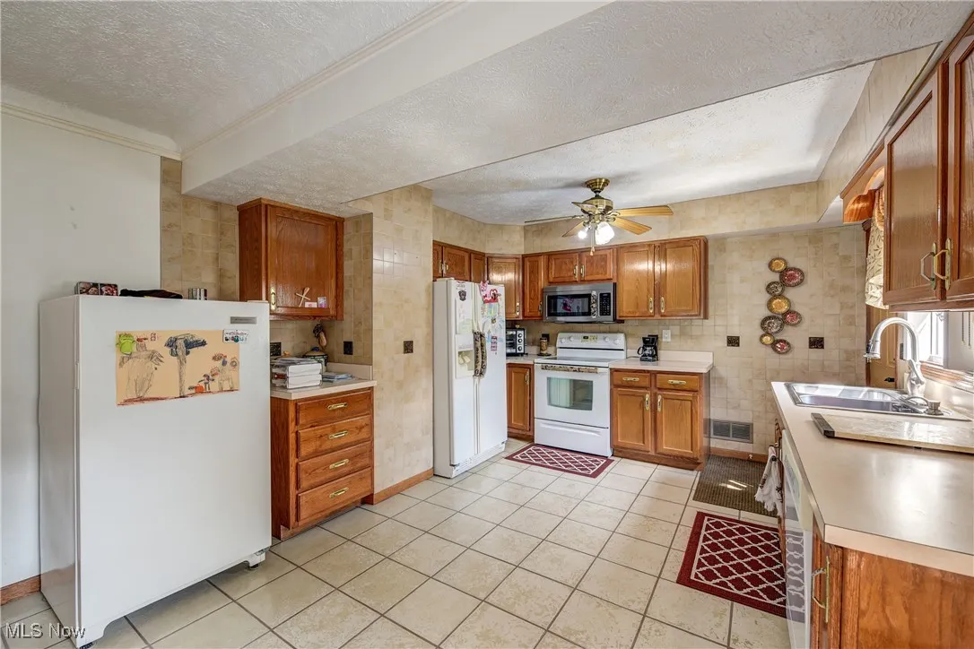 Kitchen featuring a textured ceiling, white appliances, brown cabinetry, light countertops, and light tile patterned floors