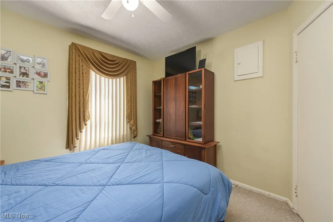 Carpeted bedroom featuring a textured ceiling, ceiling fan, and electric panel