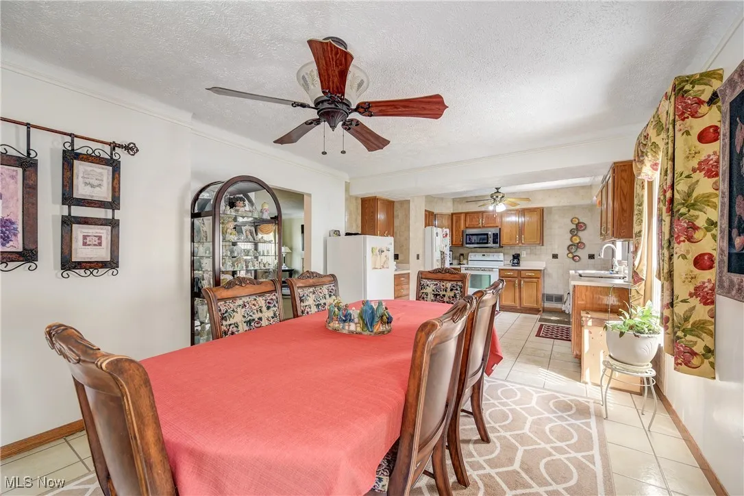 Dining area with light tile patterned floors, a ceiling fan, a textured ceiling, and ornamental molding