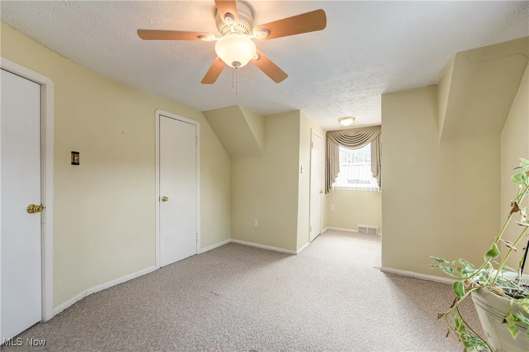 Additional living space with a textured ceiling, light colored carpet, and ceiling fan