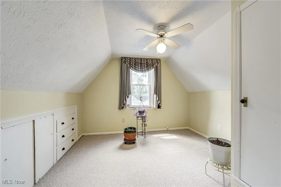 Bonus room featuring light colored carpet, vaulted ceiling, a textured ceiling, and ceiling fan