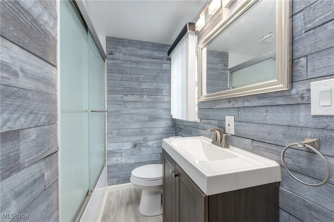 Full bath featuring vanity, an enclosed shower, tile walls, and wood finished floors