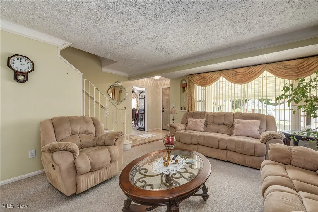 Living room featuring stairs, carpet, healthy amount of natural light, a textured ceiling, and crown molding