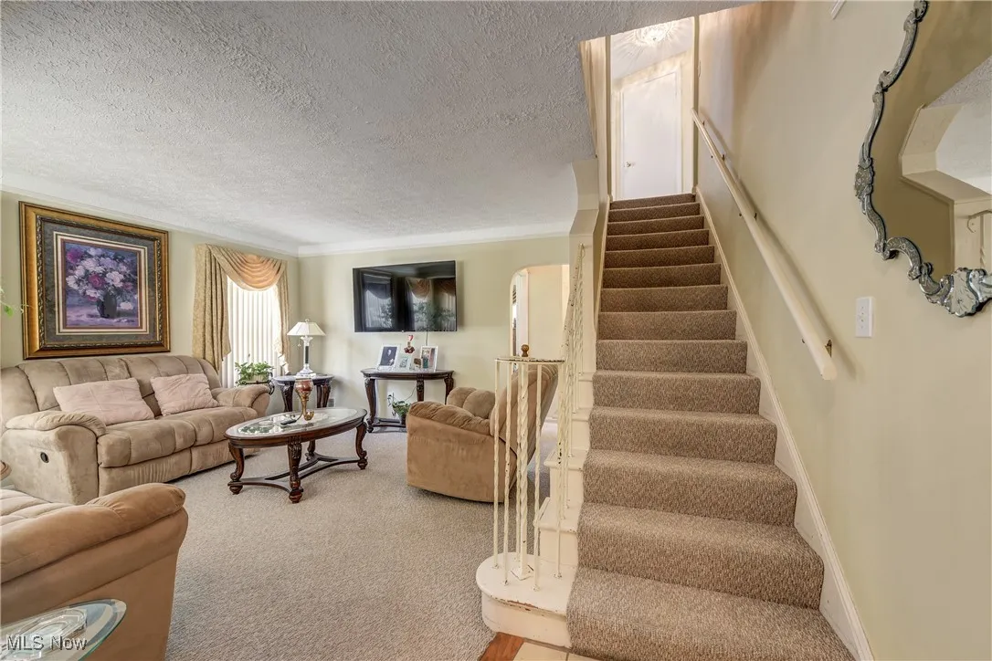 Carpeted living area with stairway, ornamental molding, a textured ceiling, and arched walkways