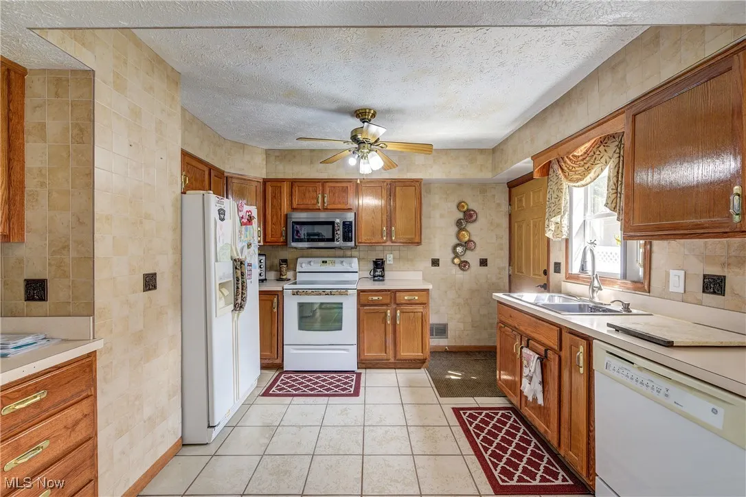 Kitchen with white appliances, a textured ceiling, light countertops, brown cabinets, and a ceiling fan