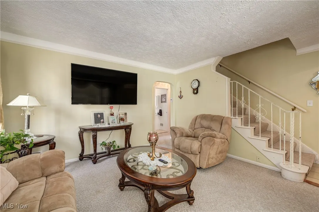 Carpeted living room with crown molding, a textured ceiling, arched walkways, and stairway