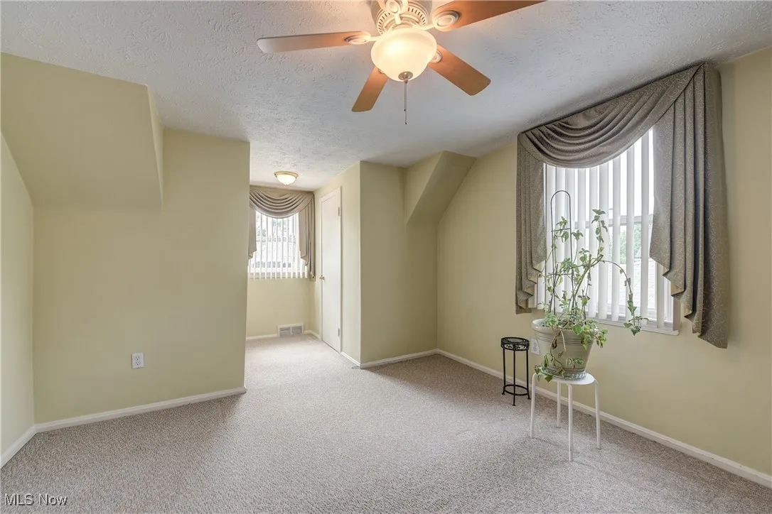 Additional living space with a textured ceiling, carpet flooring, and a ceiling fan